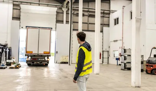 Person mit gelber Warnweste winkt LKW in Lagerhalle