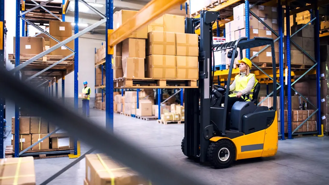 Person transportiert Kartons in Lagerhalle mit Gabelstapler