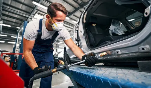 Mechaniker mit Atemschutz arbeitet an einem Auto in der Werkstatt