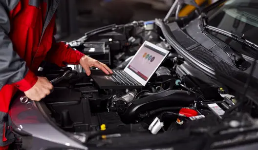 Mechaniker prüft einen Motor mit Laptop auf offener Motorhaube eines Fahrzeugs