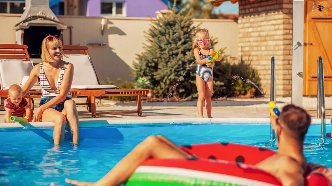 Frau mit Kindern ist am Poolrand und Mann mit Schwimmreifen im Pool