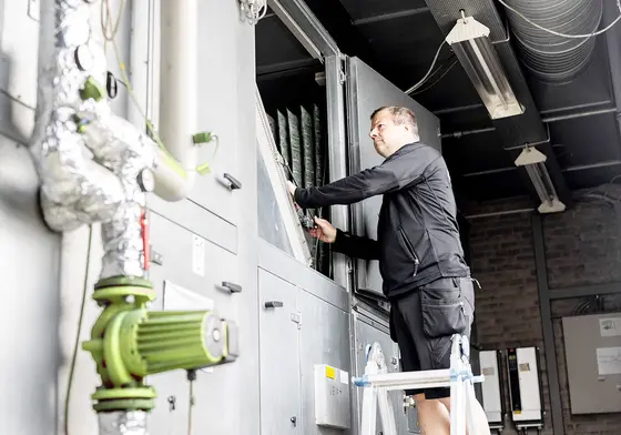 Support-Mitarbeiter steht auf Leiter und begutachtet das Innere einer Anlage