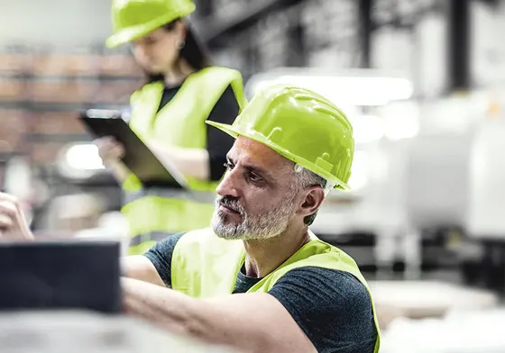 Mitarbeiter und Mitarbeiterin mit grünem Schutzhelm und Schutzweste arbeiten