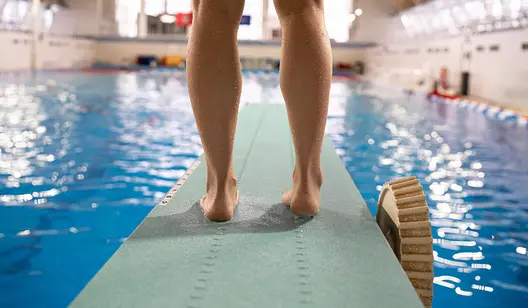 Beine auf einem Sprungbrett im Hallenbad