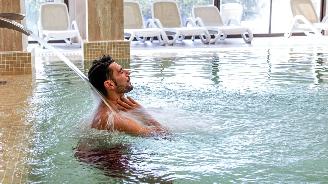 Mann steht vor Wasserstrahl im Schwimmbecken im Hallenbad