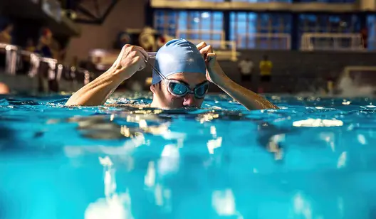 Person setzt Schwimmbrille im Wasser auf