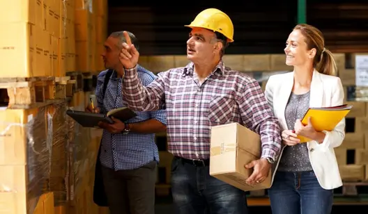 Arbeiter mit Helm führt Frau mit Mappe durch Halle