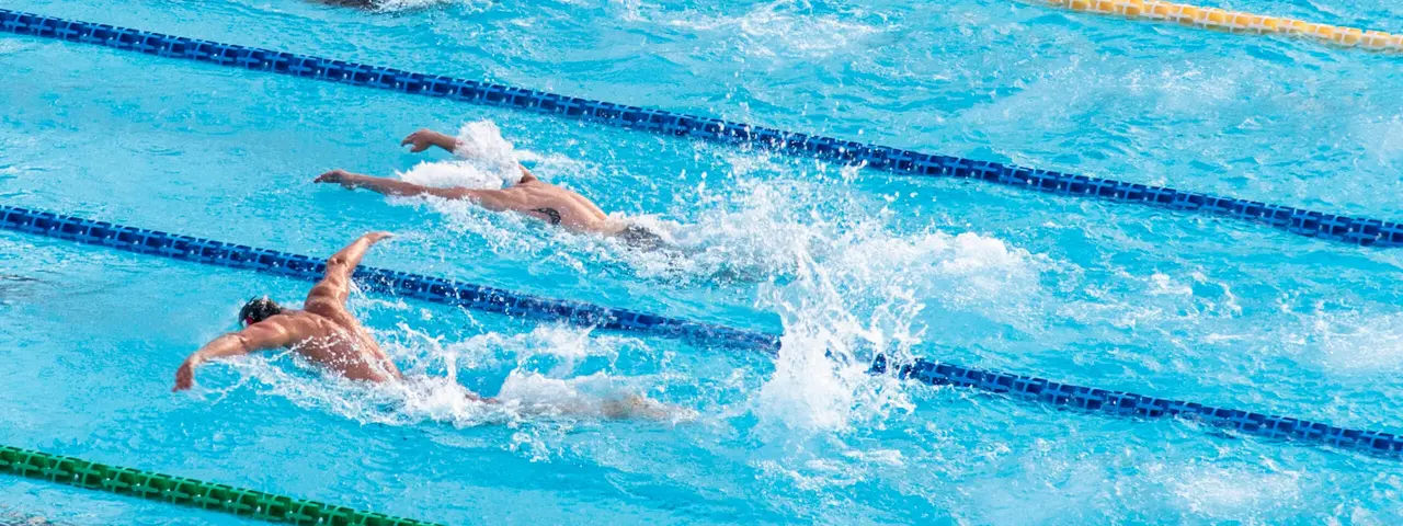 Zwei Sportler schwimmen in Bahnen im Hallenbad