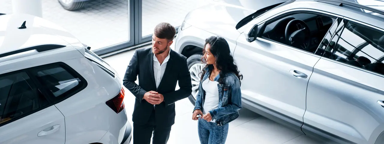 Mann und Frau stehen in belüftetem Autohaus zwischen Fahrzeugen